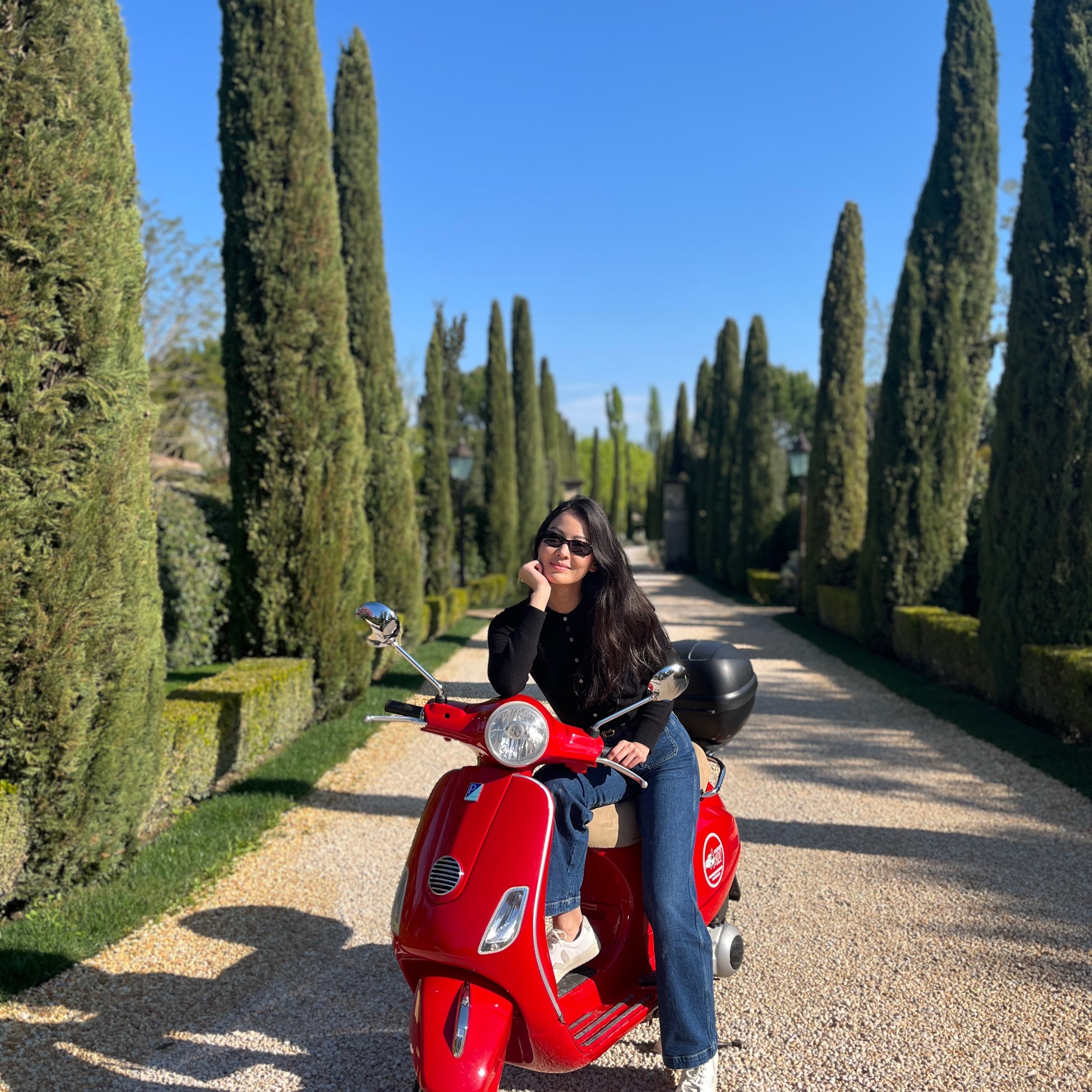 Astro Nat on a red Vespa surrounded by cypress trees